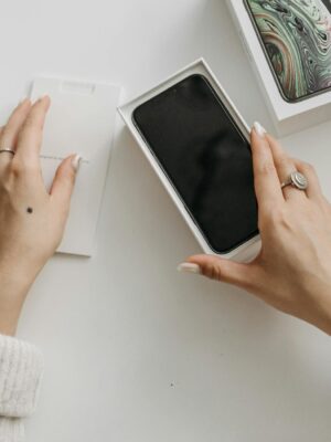 Woman unboxing a smartphone on a white table, showcasing technology and lifestyle