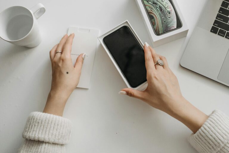 Woman unboxing a smartphone on a white table, showcasing technology and lifestyle