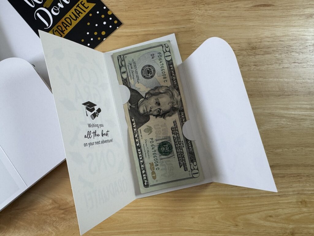 Open Decorably graduation card with a twenty dollar bill tucked into the gift slot