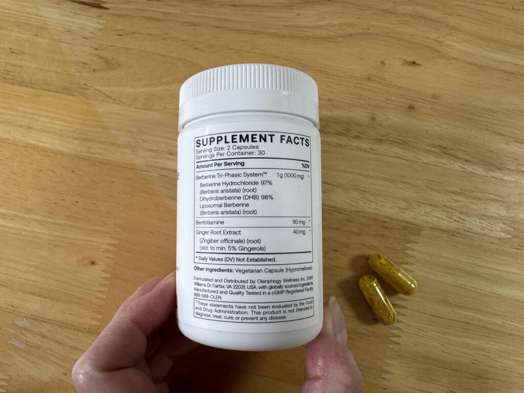 Hand holding the TriPhasic Berberine bottle to show supplement facts and two yellow capsules