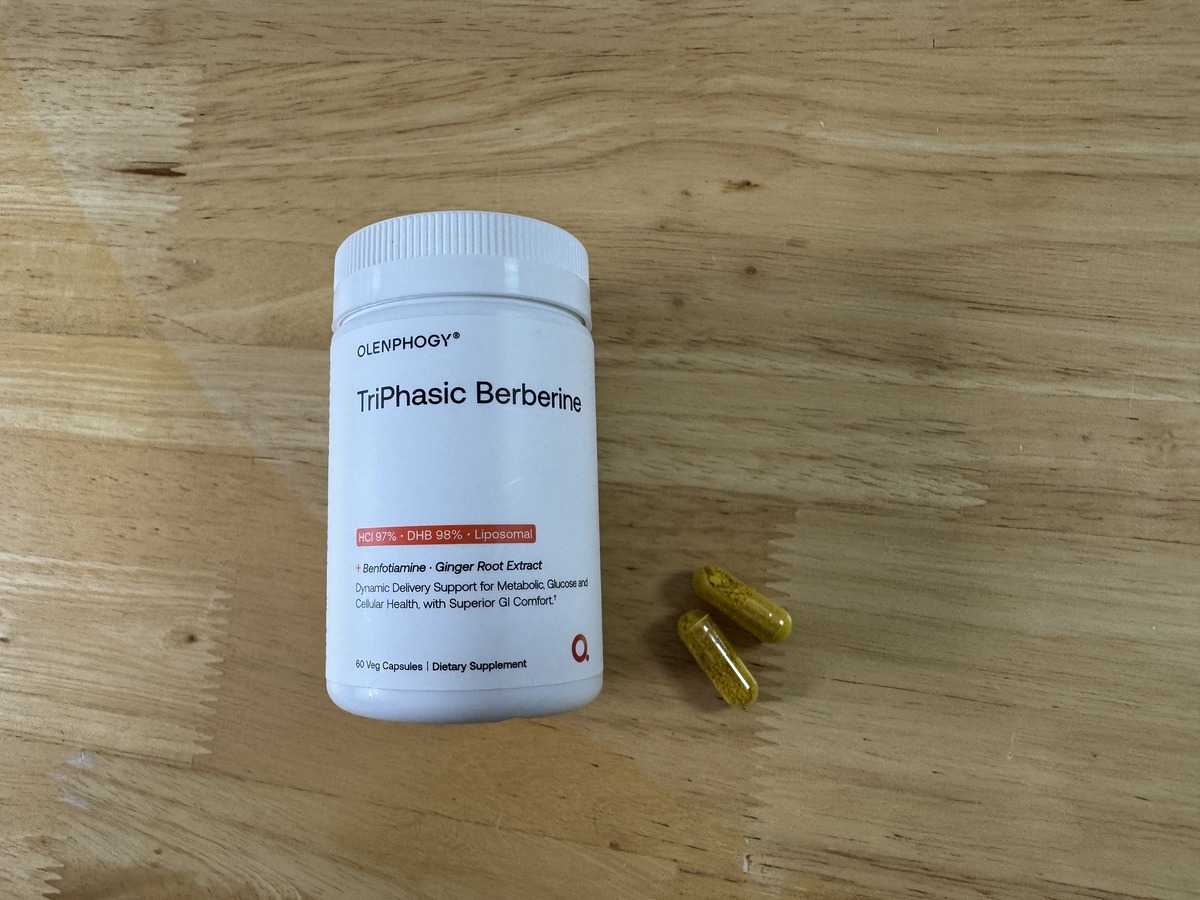 Olenphogy TriPhasic Berberine bottle on a wood surface with three yellow capsules beside it
