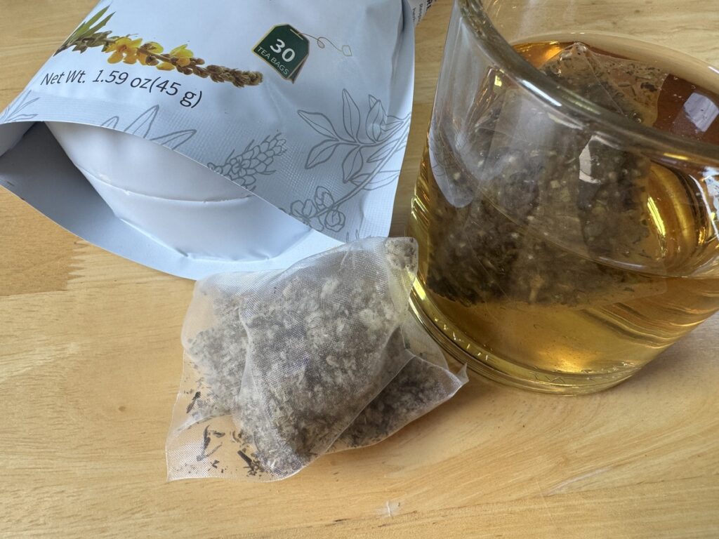 Respira Botanicals Mullein Leaf Tea pouch beside a glass cup of brewed tea and a tea sachet on a wood surface