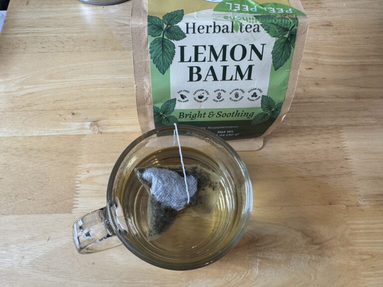 Glass mug of brewed Hihone Lemon Balm herbal tea beside the green foil pouch on a wood table