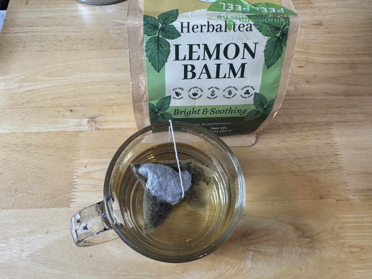 Glass mug of brewed Hihone Lemon Balm herbal tea beside the green foil pouch on a wood table