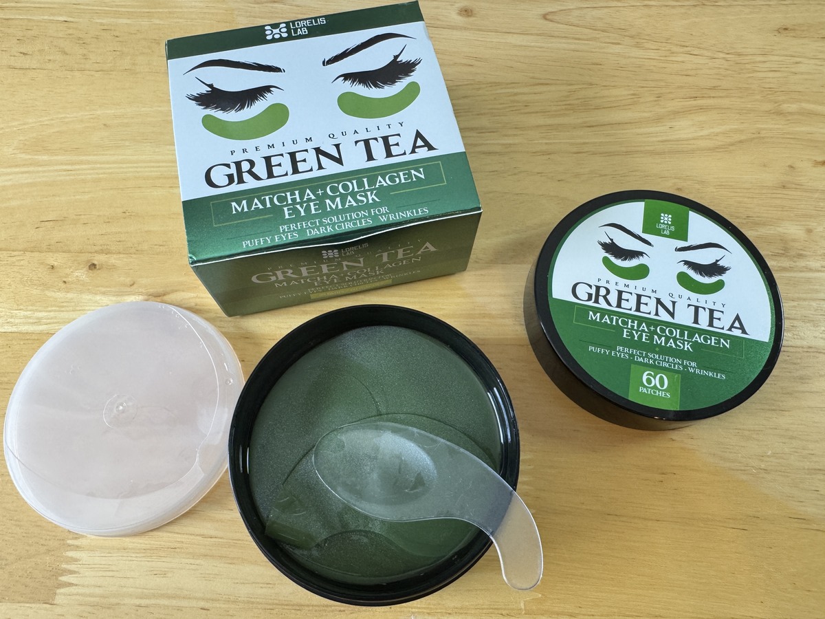 Open jar of Green Tea Matcha Collagen Eye Mask patches with applicator spoon and product boxes on wood