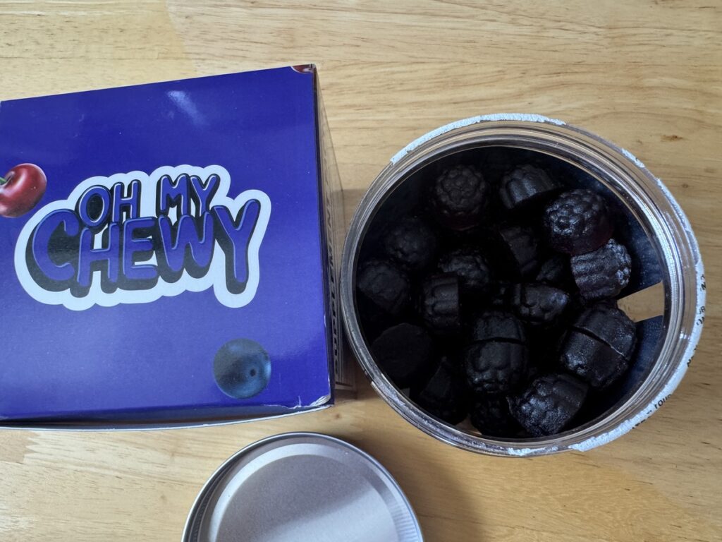 Oh My Chewy Calm and Sleep Gummies purple box and open jar of tart cherry and grape gummies on a wood counter