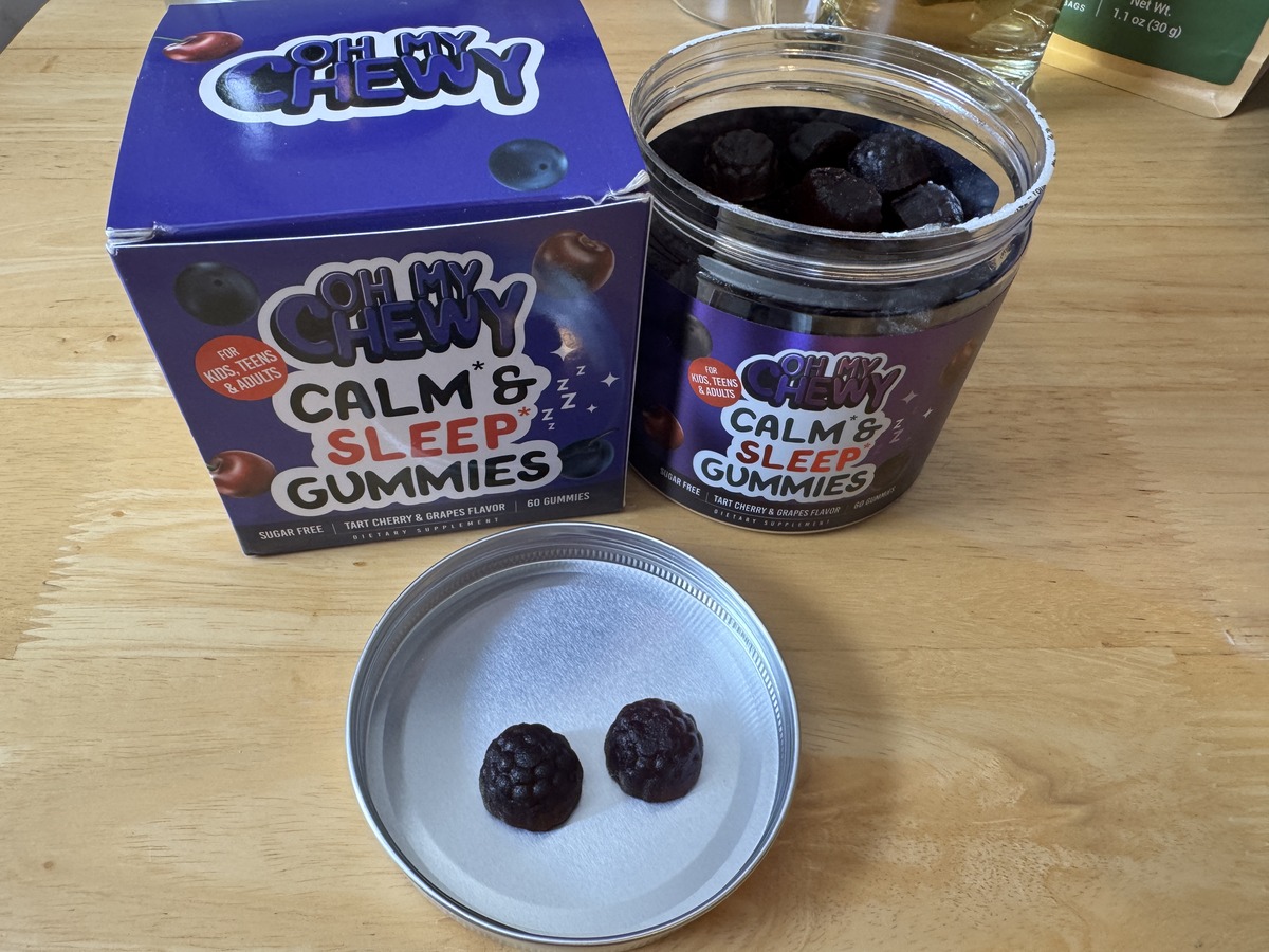 Two Oh My Chewy Calm and Sleep Gummies in tart cherry and grape flavor on a metal jar lid next to the box