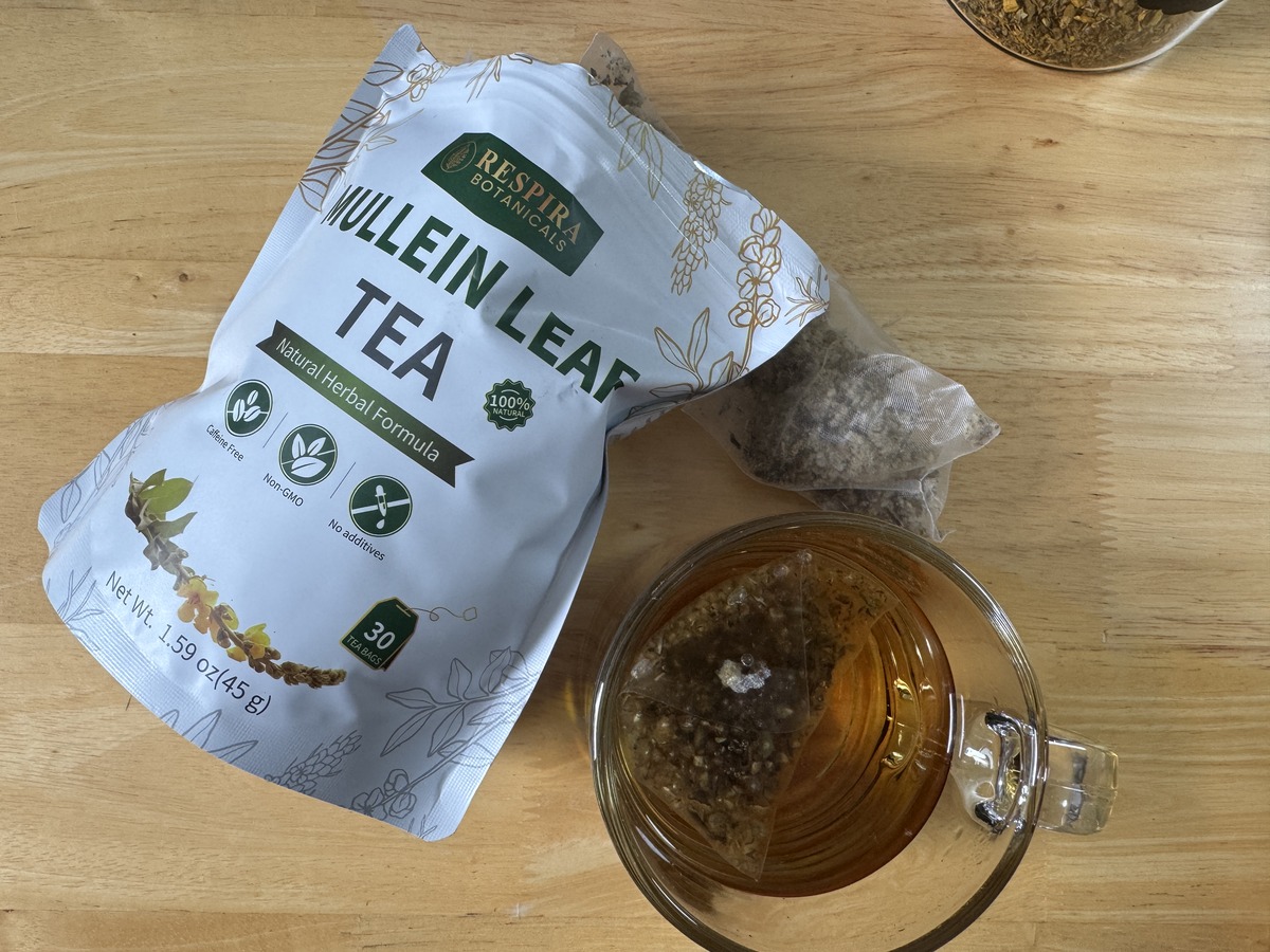 Open 1.59 oz foil pouch of herbal tea with 30 bags beside two pyramid sachets and a glass cup of brewed tea