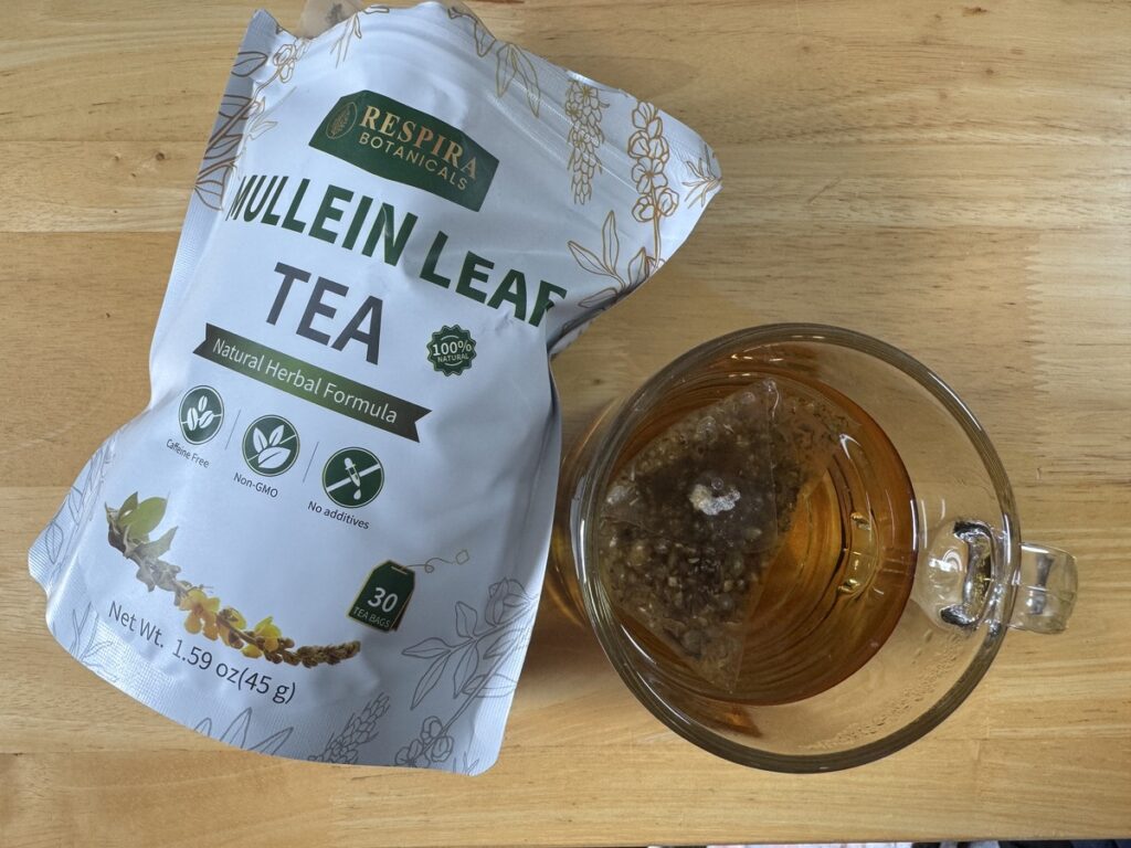 Respira Botanicals Mullein Leaf Tea pouch next to a glass cup of brewed tea on a wood table