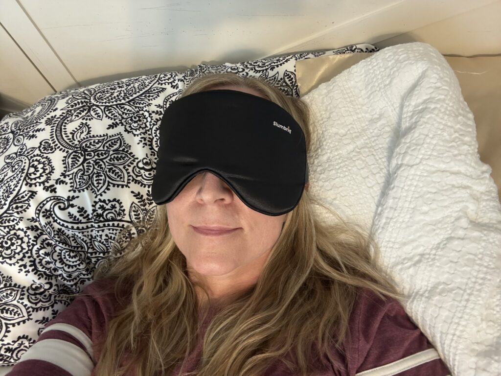 Woman lying on a paisley pillow wearing a black Slumbriq sleep mask over her eyes