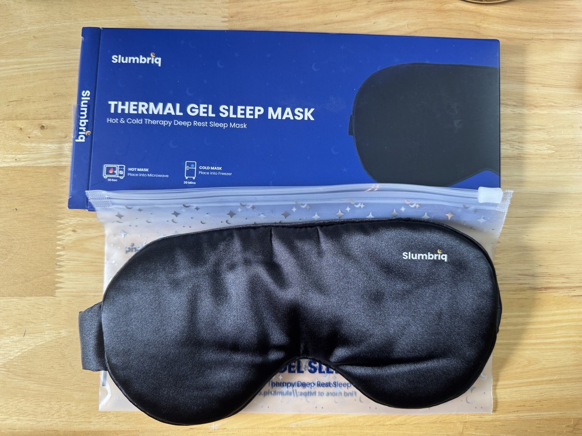 Slumbriq Thermal Gel Sleep Mask in black satin next to its blue retail box on a wood surface