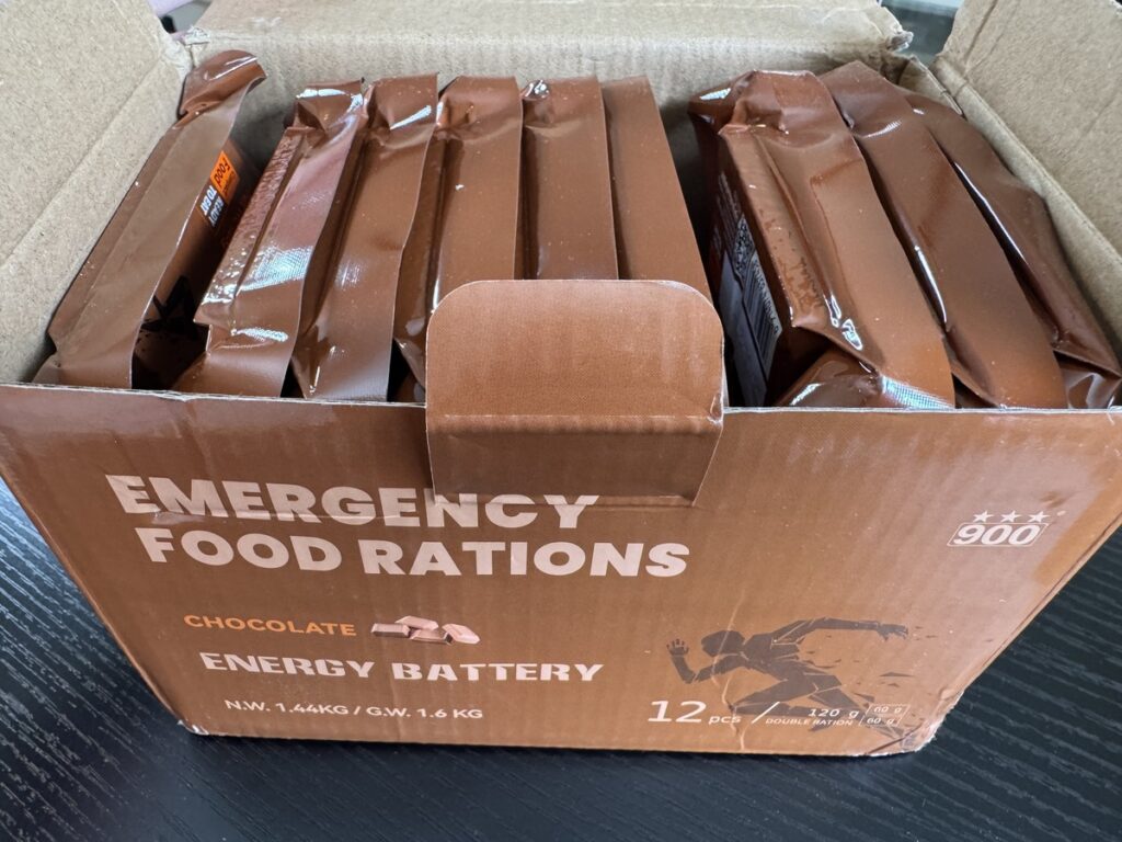 Open case of Emergency Food Rations Chocolate Energy Battery 900 with 12 individually wrapped brown foil bars inside.