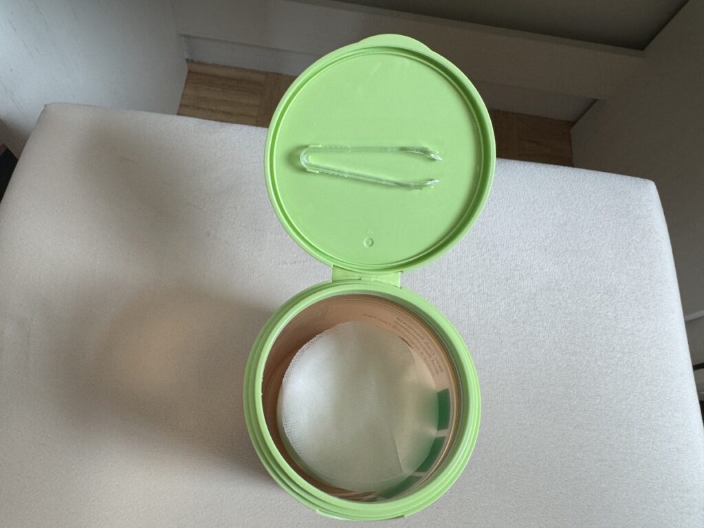 Open empty round lime green plastic storage container with hinged lid on white surface.