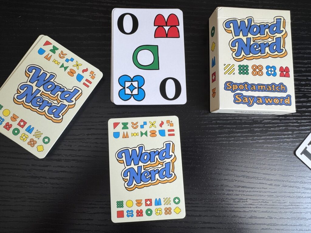 Word Nerd card game box with tagline Spot a match Say a word next to three cards on a dark wood table.