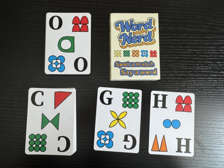Word Nerd card game box with four letter cards showing O, C, G, and H spread on a dark wood table.