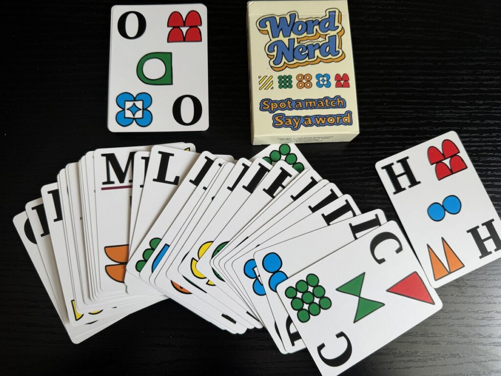 Word Nerd card game box with cards spread across a dark table showing letters and colorful symbol icons.