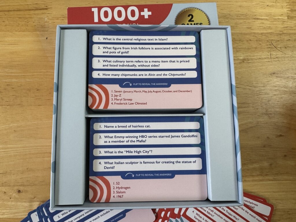 Open trivia game box showing two decks of question cards on religion, culture, and animals with a 1000+ questions label.