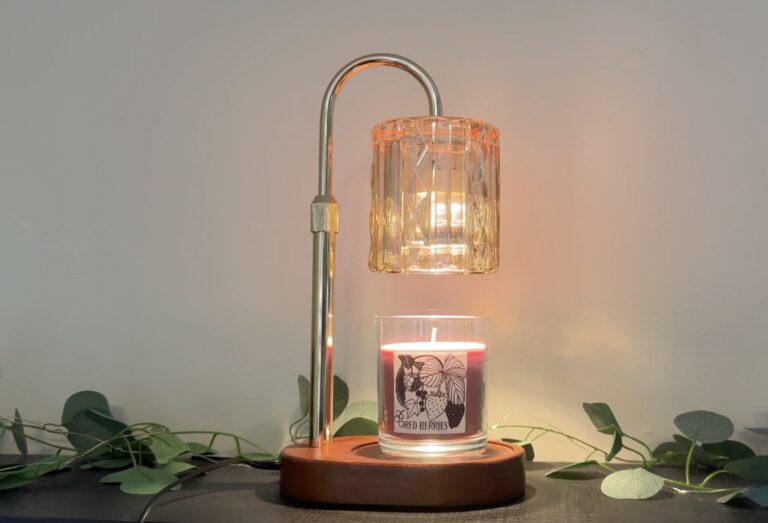 Brass arched candle warmer lamp with fluted glass shade warming a Red Berries candle on a wooden base with eucalyptus.