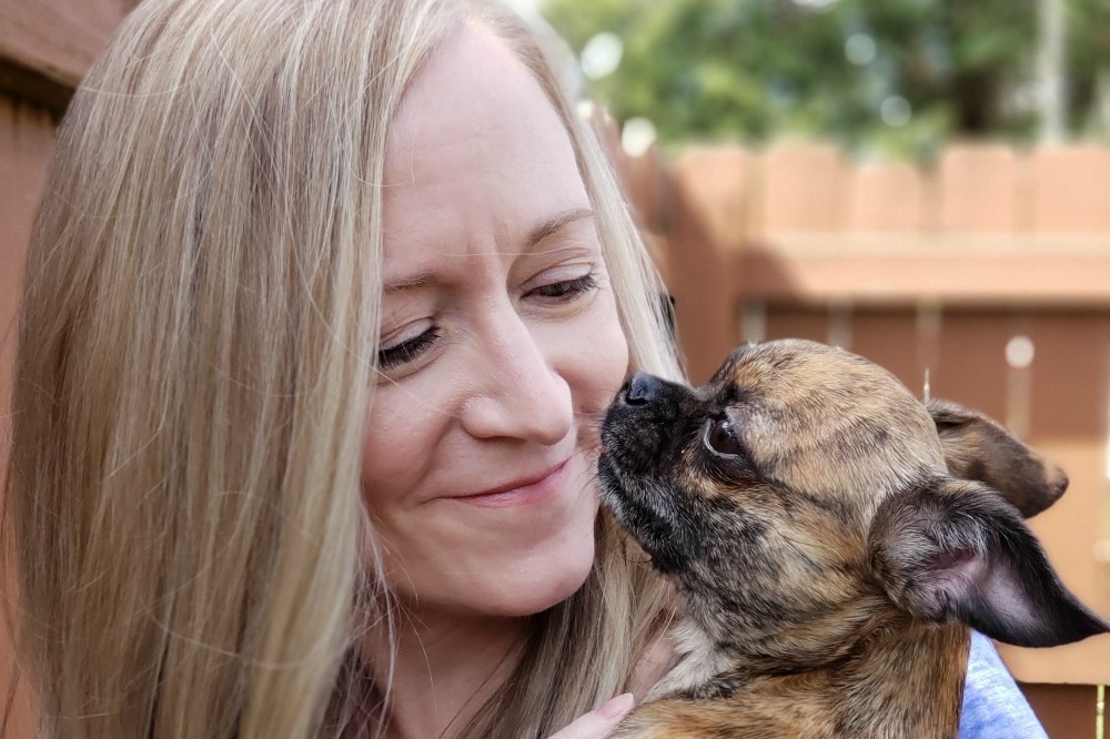 Jen holding her rescue dog Little Bits, who is licking her face