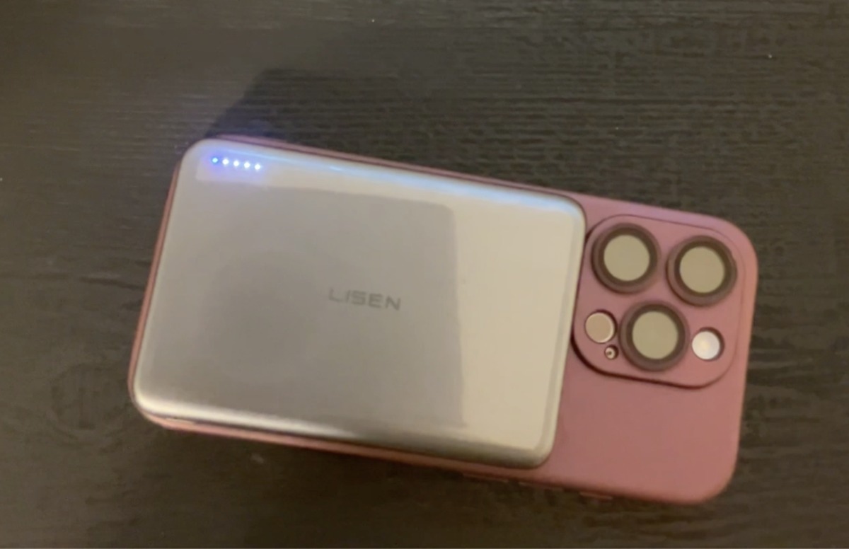 Jen holds up a black Lisen Phone Accessories power bank box with purple branding in a bedroom.