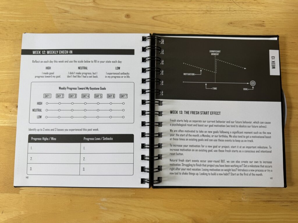 Open spiral-bound workbook on a wood surface showing Week 12 Weekly Check-In and Week 13 The Fresh Start Effect pages.
