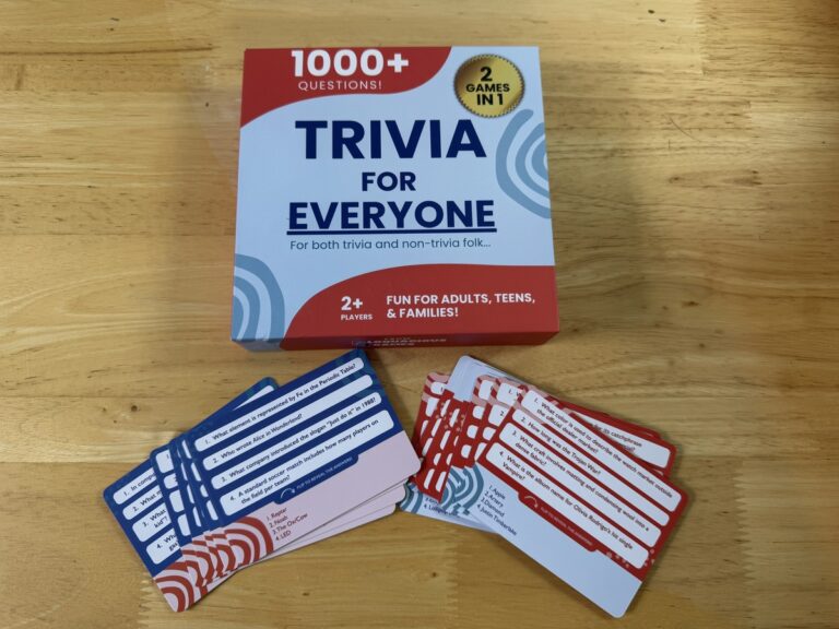 Trivia For Everyone 1000+ Questions 2-Games-in-1 box beside two fanned stacks of blue and red question cards on a wood table.