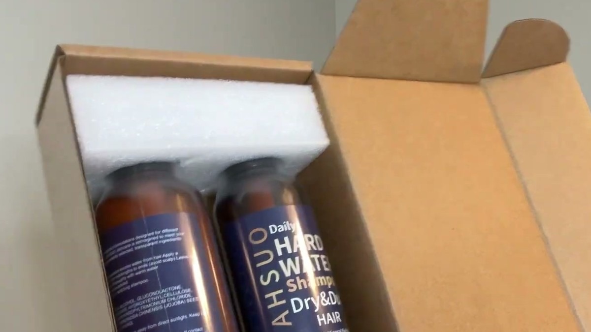 AHSUO hard water shampoo and conditioner set in its open box, both bottles nested in white foam with the product guide alongside