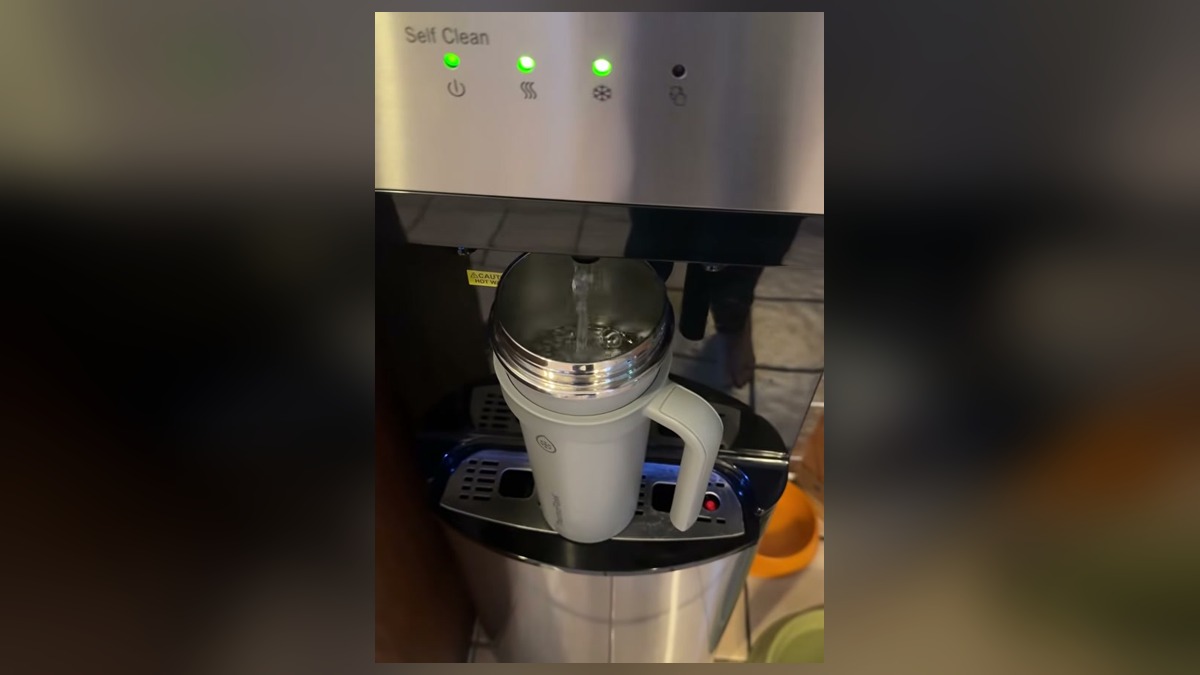 Water pouring from the Brio bottom loading dispenser into a tall gray tumbler standing on the drip tray without tilting