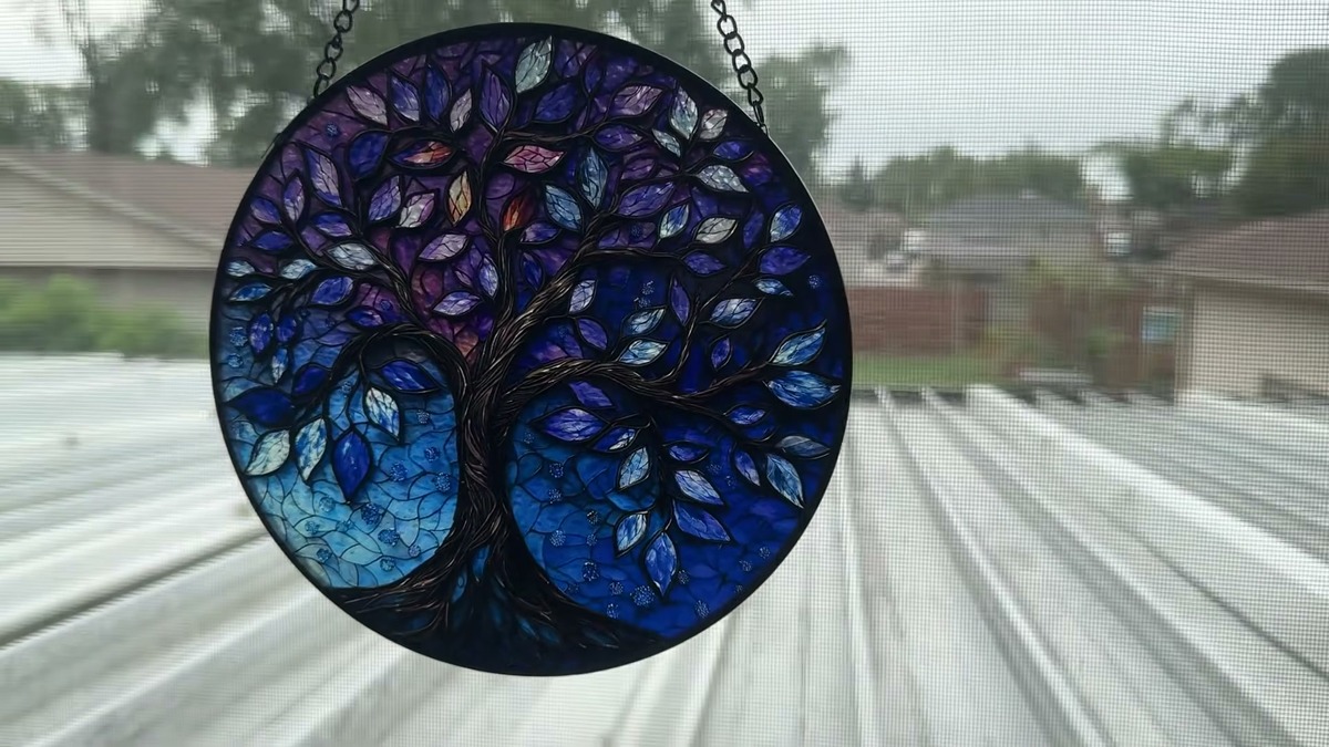DASTOLL Tree of Life suncatcher hanging on its chain in an office window with a porch roof behind it
