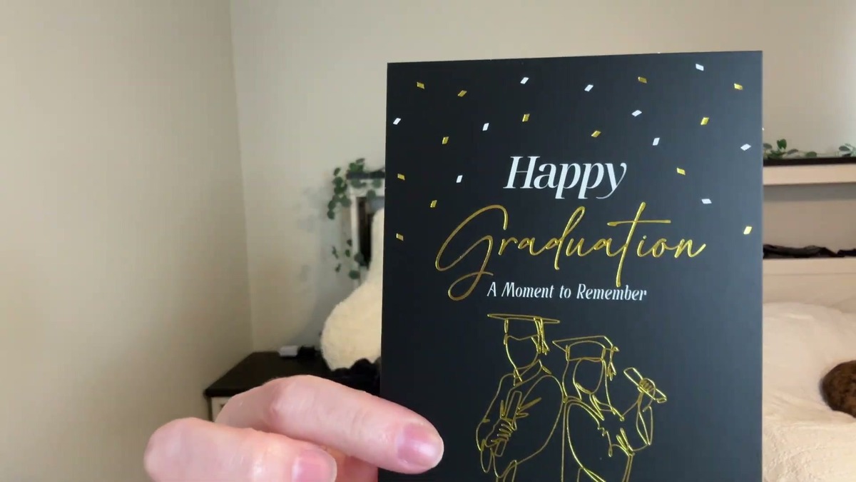 A black Decorably graduation card with gold foil Happy Graduation lettering and a line drawing of two graduates