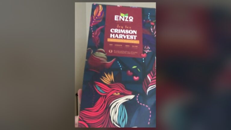 ENZO Crimson Harvest herbal tea box, navy with a red fox and cherries on the front, held up in front of a blurred wall