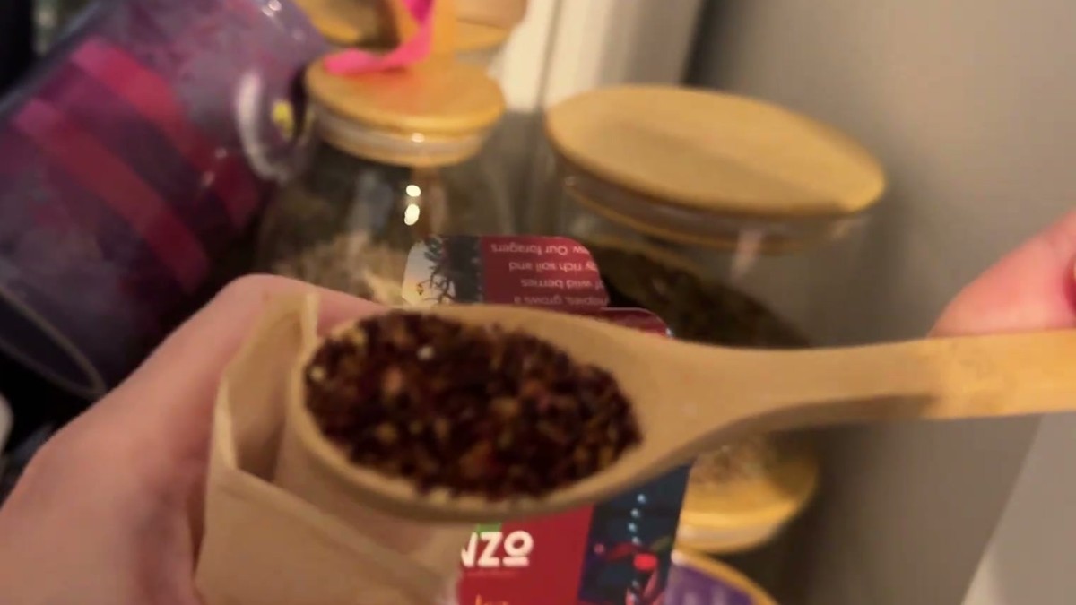 Wooden scoop of fine dark red ENZO Crimson Harvest loose leaf tea being poured into a fill-your-own paper tea bag