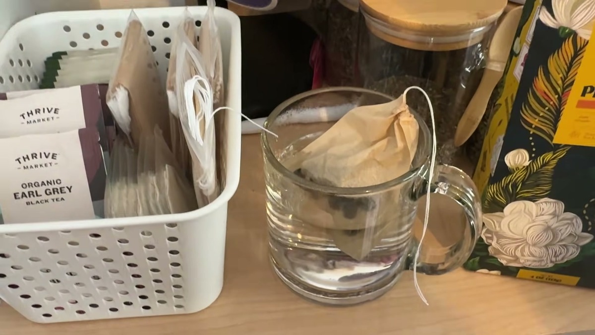 Fill-your-own tea bag of Enzo jasmine pearls steeping in a glass mug on the counter, pale gold tea