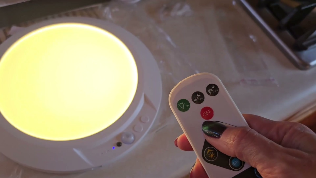 Fsaox magnetic ceiling light lit in warm white on a counter with the included remote held next to it