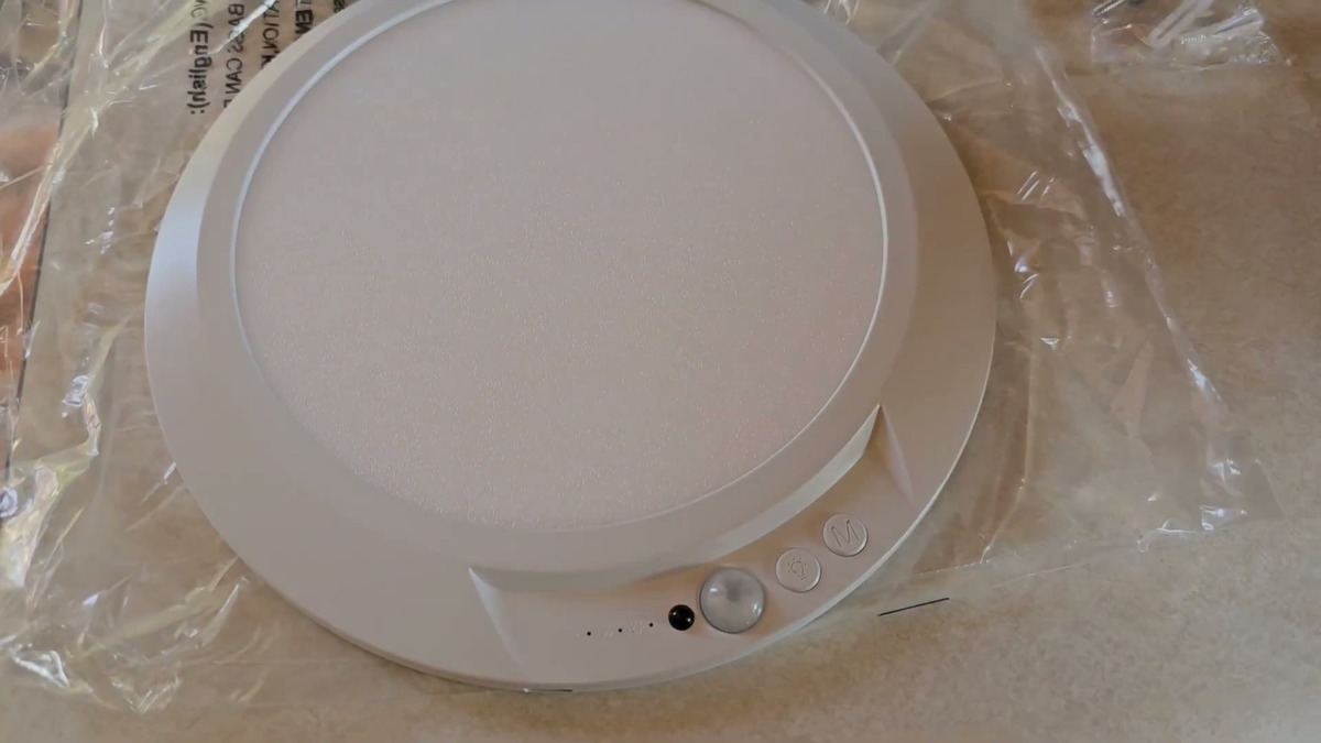 Fsaox rechargeable motion sensor ceiling light, a white round LED panel with the motion sensor and two buttons on the rim, out of the box on a counter