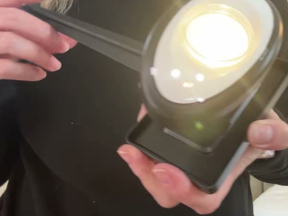 Fuligent solar spotlight held in two hands and glowing warm white, with the ground stake and square solar panel attached