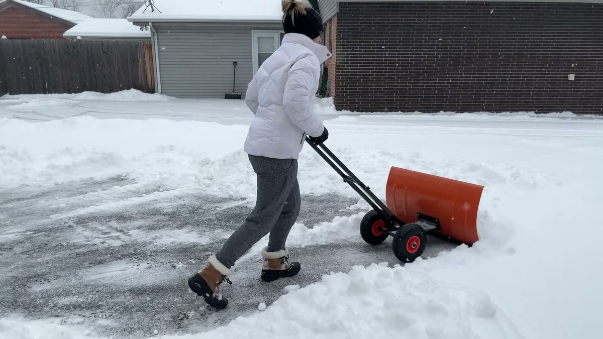 Garvee wheeled snow shovel clearing a full-width path through several inches of light snow on a driveway while it is still snowing