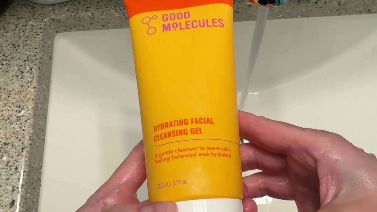 Good Molecules Hydrating Facial Cleansing Gel in its orange and yellow 6.7 oz tube, held over a bathroom sink