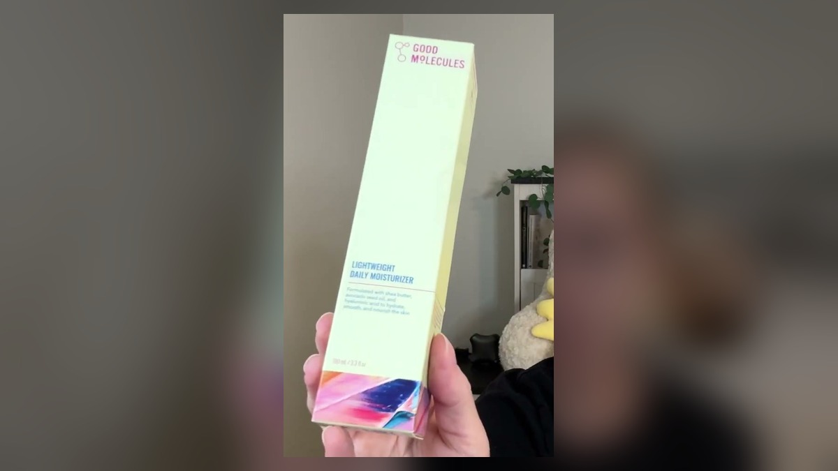 Pale green Good Molecules Lightweight Daily Moisturizer box with a colorful painted stripe at the bottom, held up in one hand