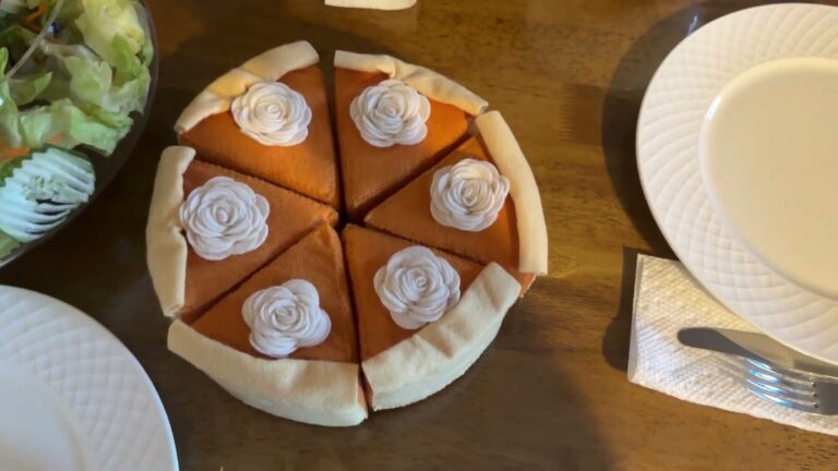 Six Hahafelt felt pumpkin pie slices pushed together into one whole pie on a wooden dining table, each slice topped with a white felt whipped cream rosette