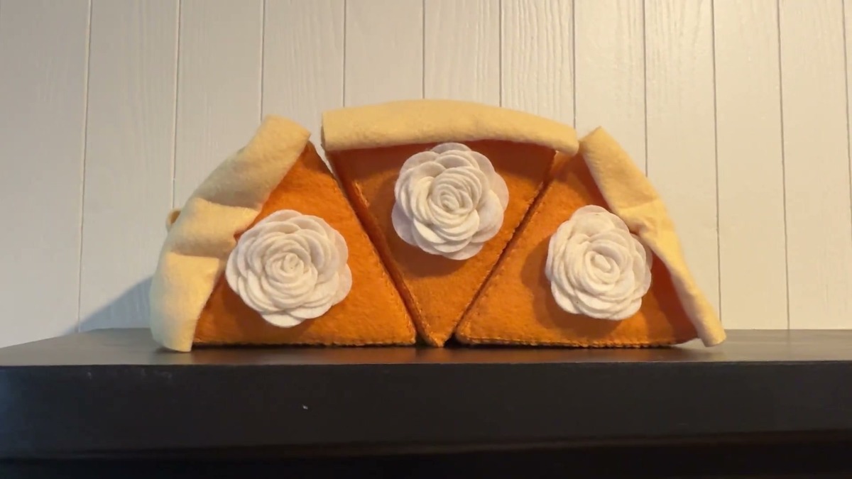 Three Hahafelt felt pumpkin pie slices standing side by side on a black fireplace mantel against a white paneled wall
