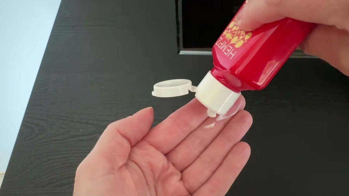 Lotion squeezed from the flip cap of a red Hempz Mini Honeycrisp Apple and Cherry Chai bottle into an open hand