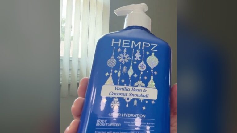 Hempz Vanilla Bean and Coconut Snowball body moisturizer, a blue 12 oz pump bottle with silver holiday ornament graphics, held up in front of window blinds