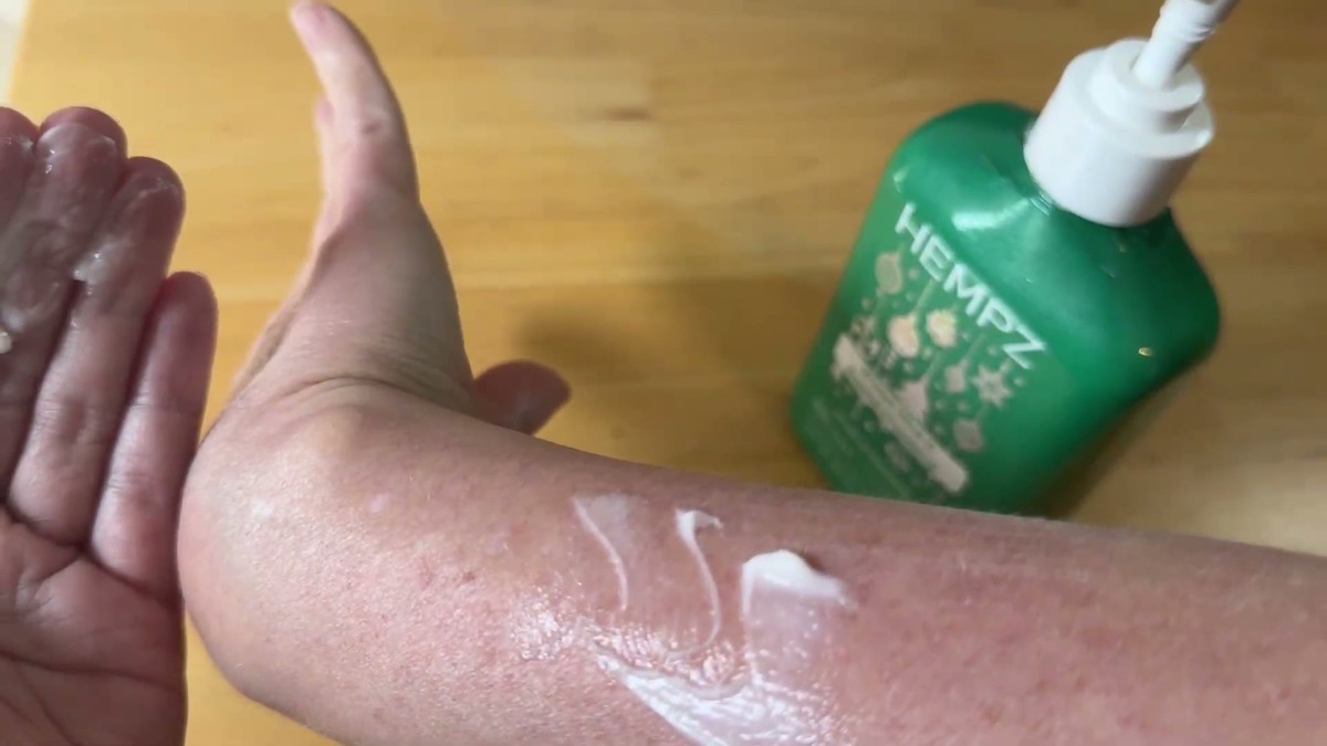 Hempz Winter Mint lotion being smoothed onto a sun-dried forearm with visible dry lines, green bottle in the background