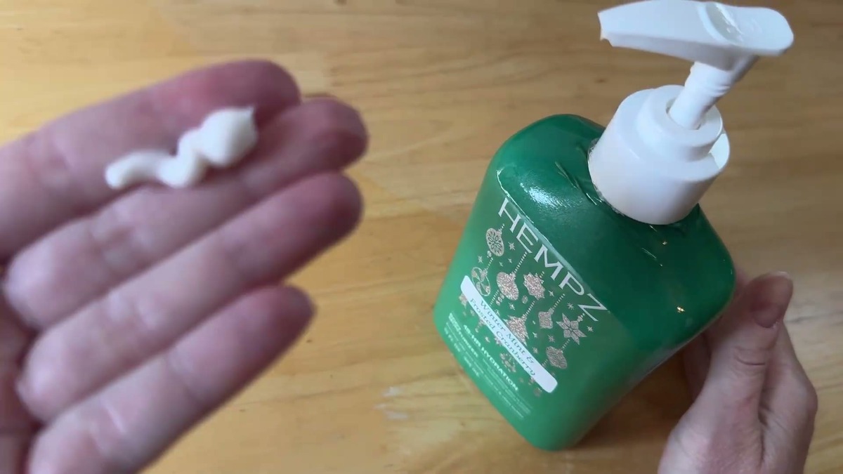 A pump of white Hempz Winter Mint lotion in an open palm next to the green bottle, showing the lightweight texture