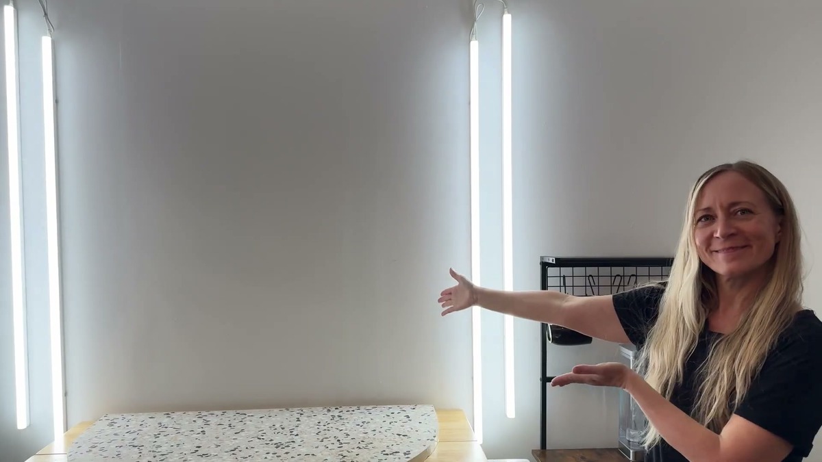 Jen smiling and pointing to the lit Pak LED shop lights she mounted vertically around her office photo area