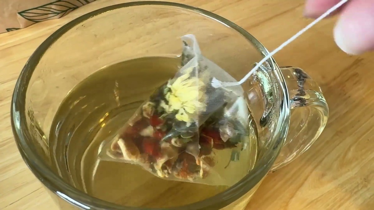 Liver and kidney detox tea bag steeping in a glass mug, the chrysanthemum opened and the water turning pale gold