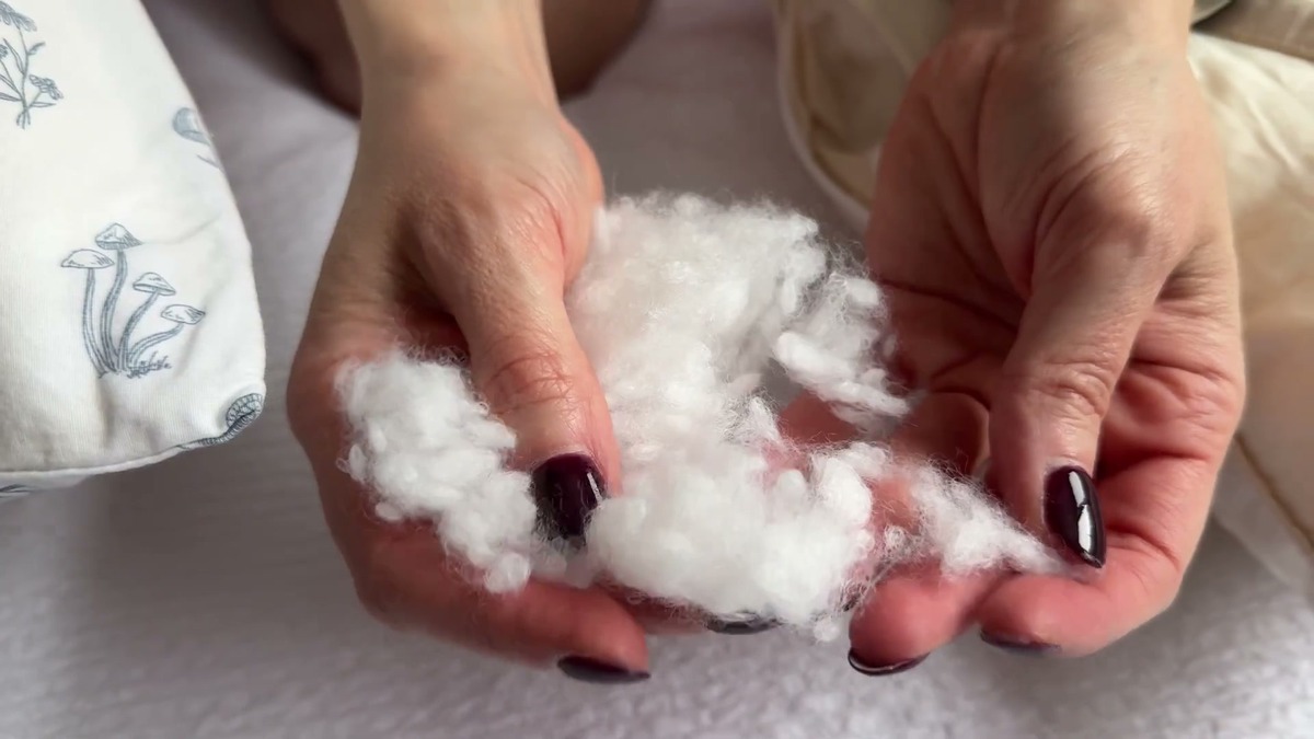 Two hands holding a loose puff of the LOFE pillow's white pearl fiber fill pulled out through the side zipper