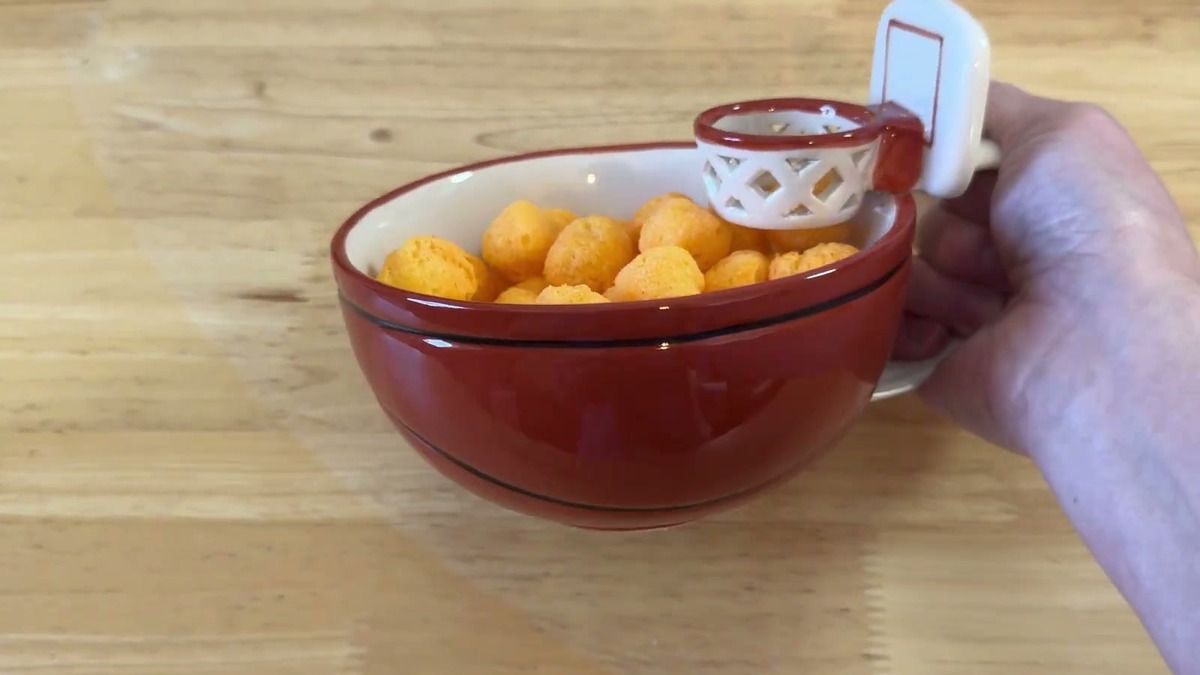 Side view of the red basketball-print MAX'IS Creations mug held by its handle, showing the wide bowl shape and the hoop on the rim