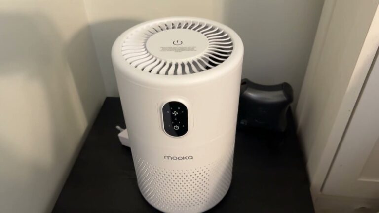 White MOOKA B-D02L air purifier sitting on a small black end table, with its round top fan grille and front touch control panel in view
